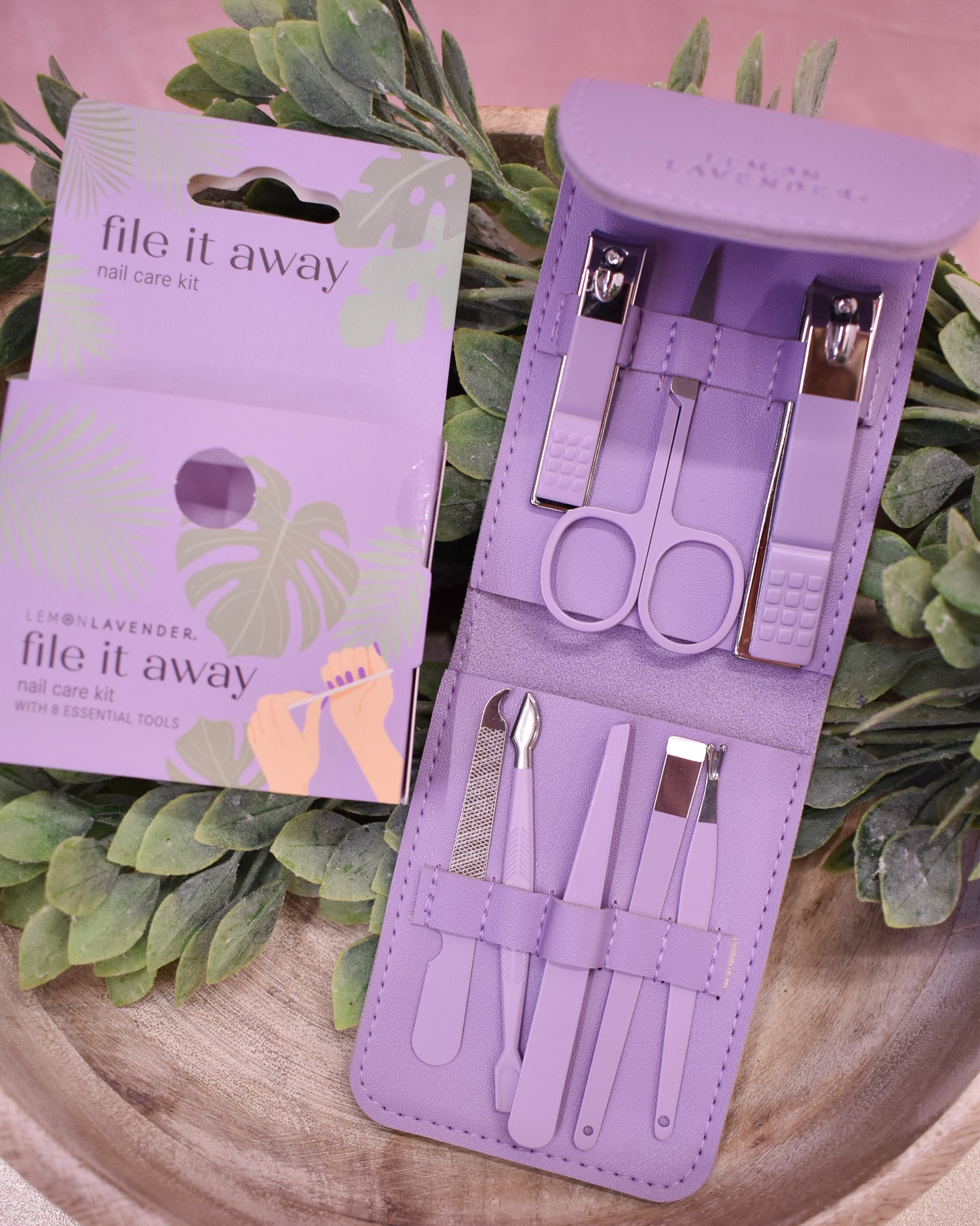 Purple nail care kit with tools and packaging on a green leafy background