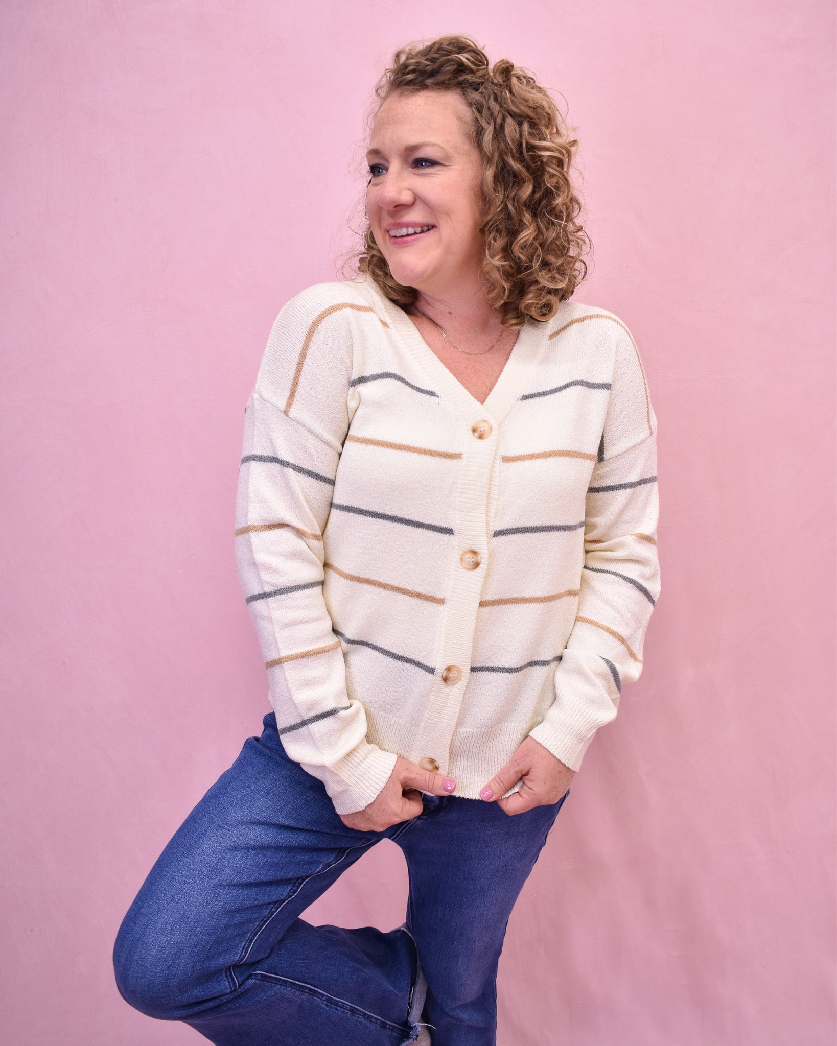 Woman wearing a striped cardigan and blue jeans against a pink background