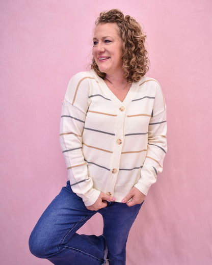 Woman wearing a striped cardigan and blue jeans against a pink background
