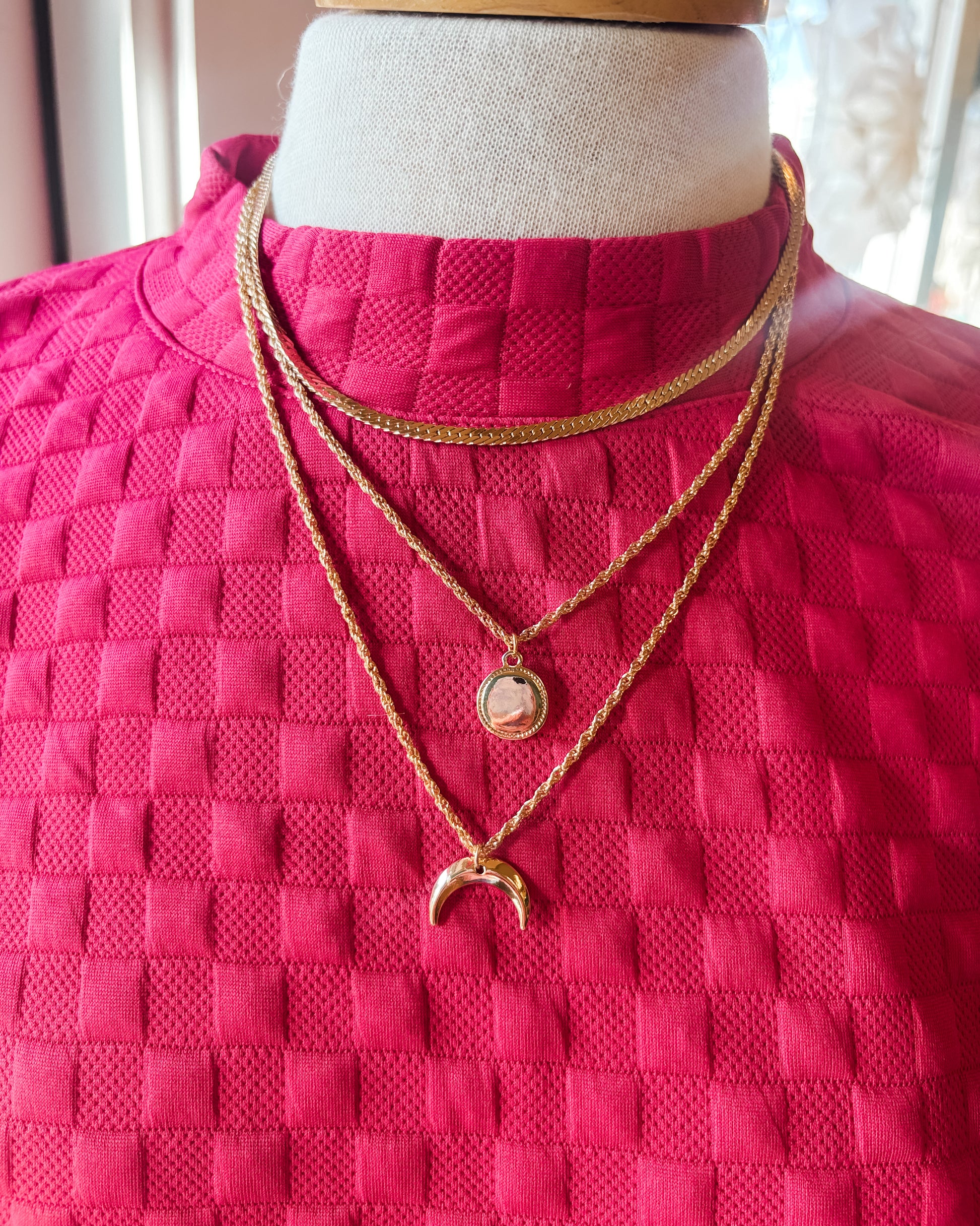 Mannequin wearing a bright pink textured garment with gold necklaces.