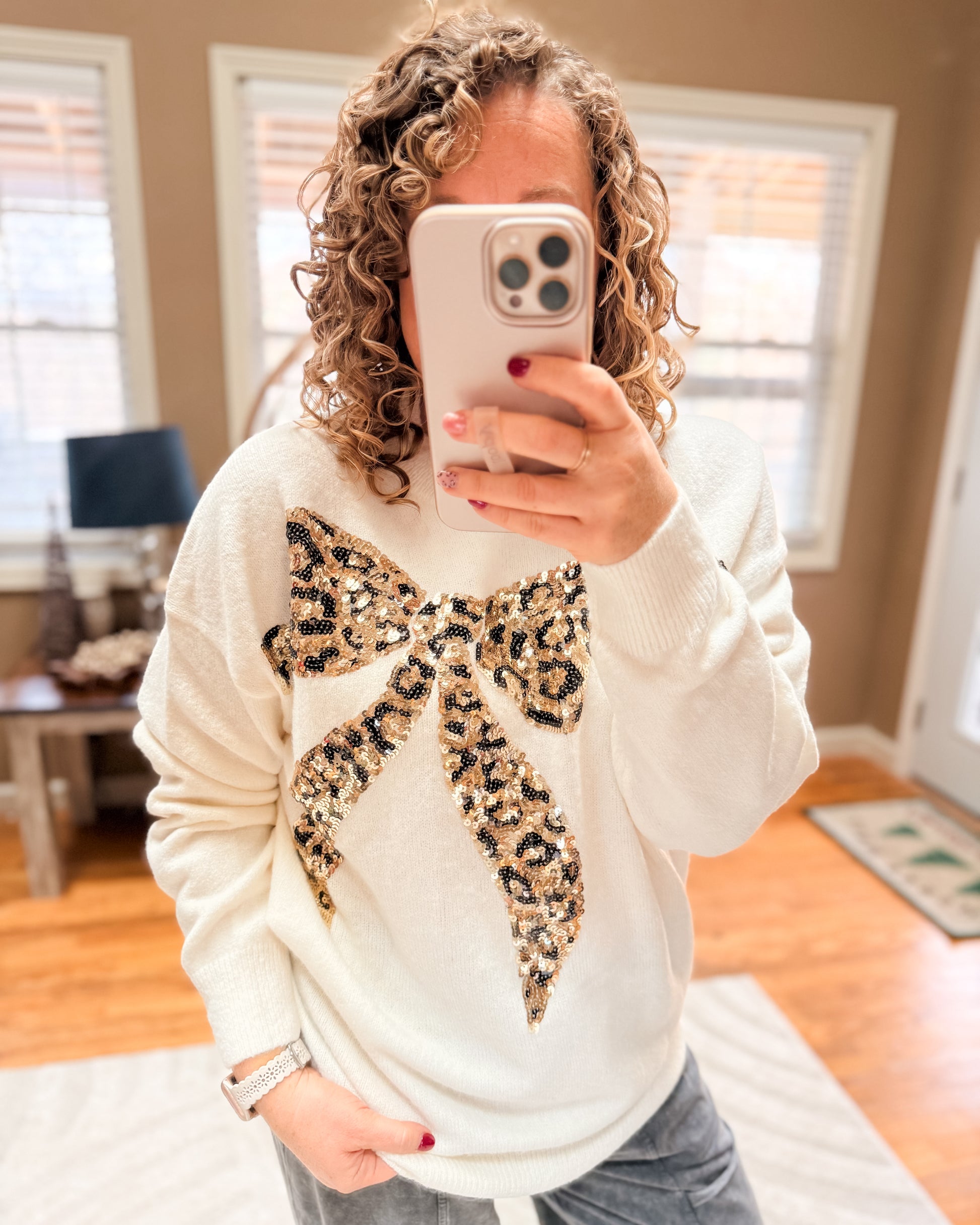 Person wearing a white sweater with a leopard print bow in a room.