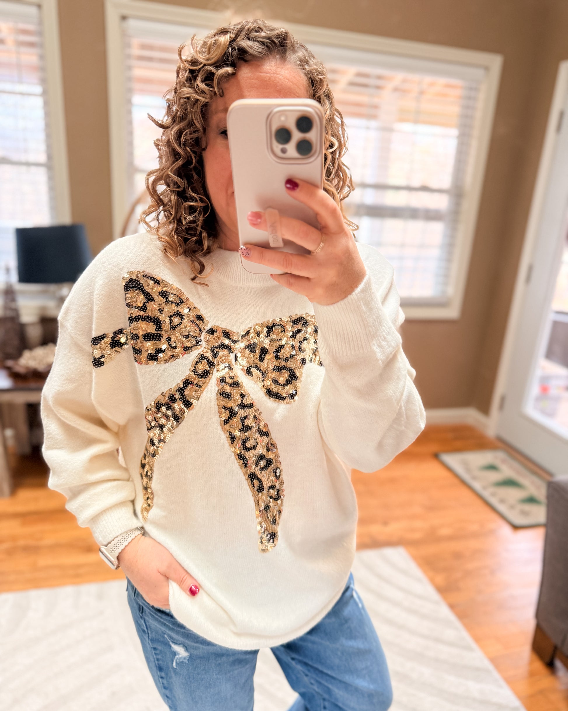 Person wearing a white sweatshirt with a leopard print bow design, taking a mirror selfie.