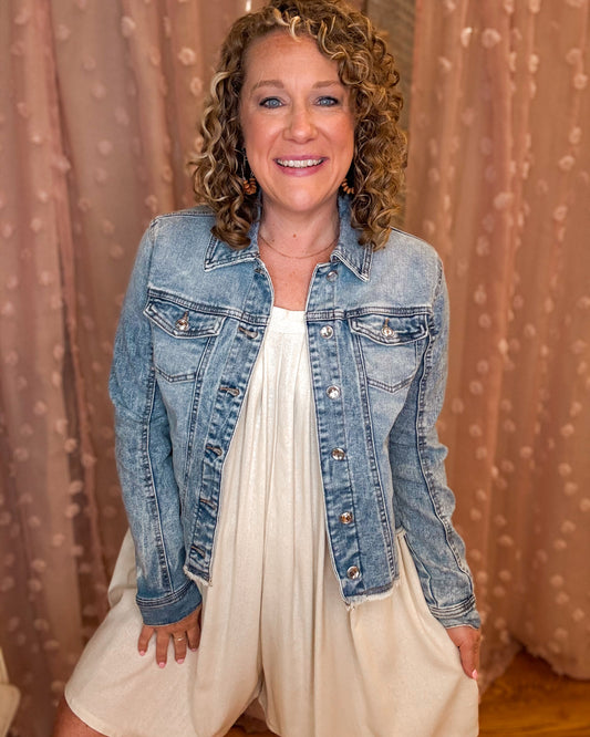 Woman wearing a denim jacket over a white dress against a beige curtain background