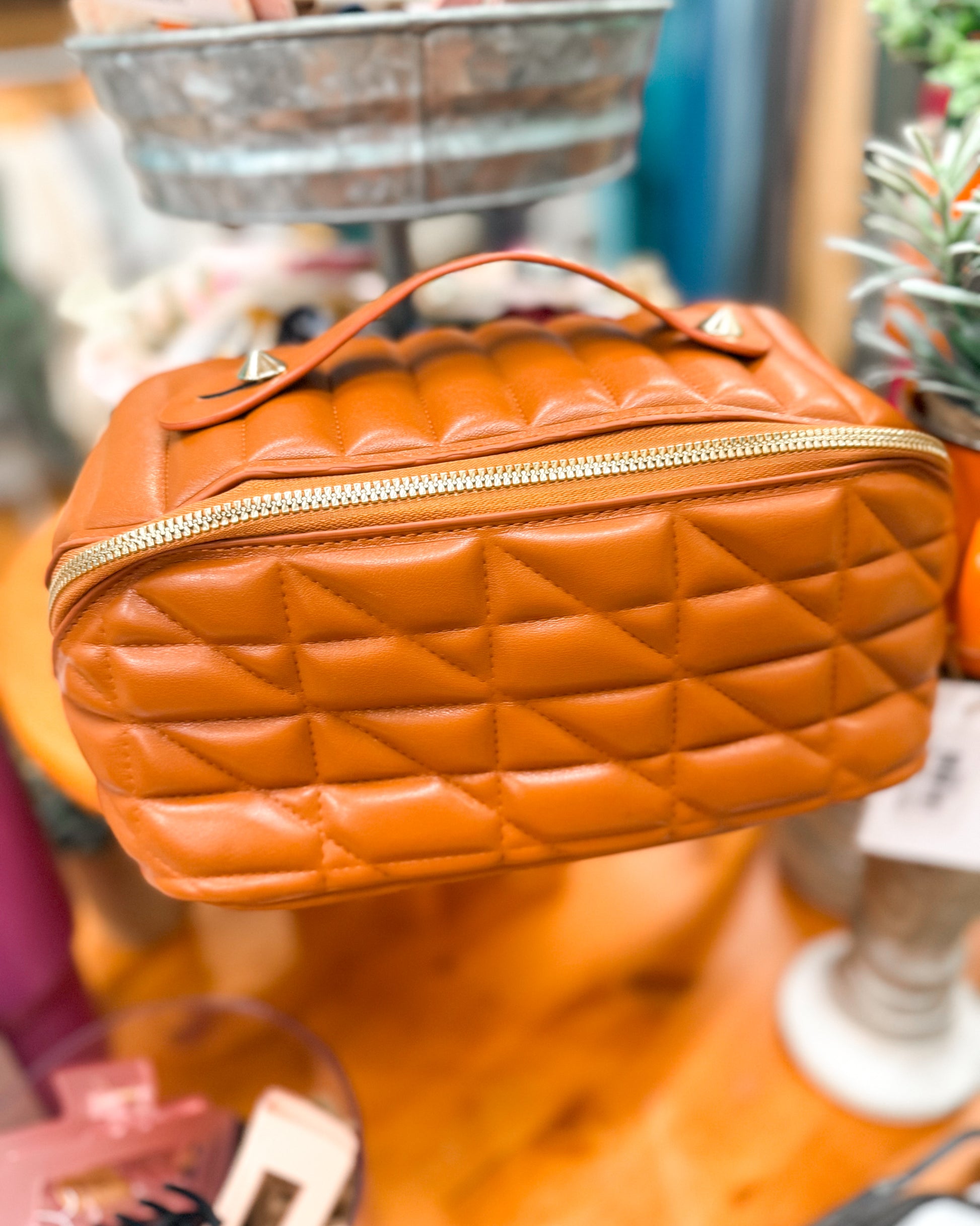 Orange quilted handbag with gold zipper on a blurred background