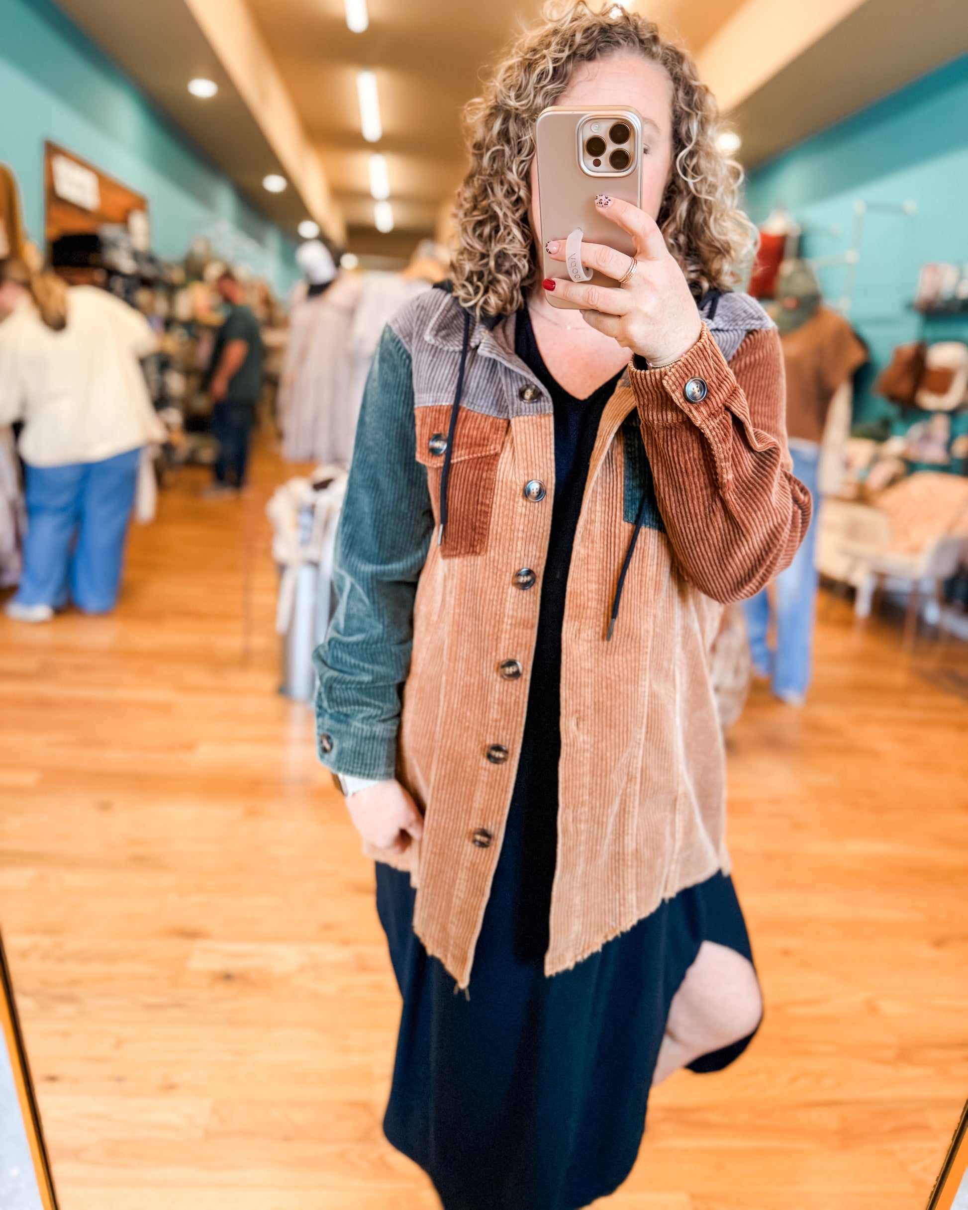 Person taking a mirror selfie wearing a patchwork jacket in a store.