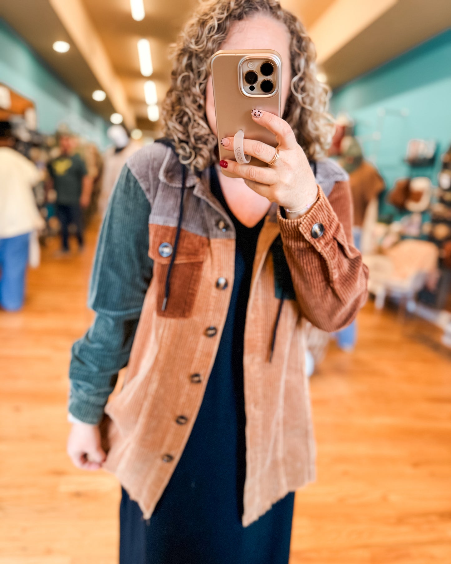 Person taking a mirror selfie wearing a brown and blue jacket in a store.