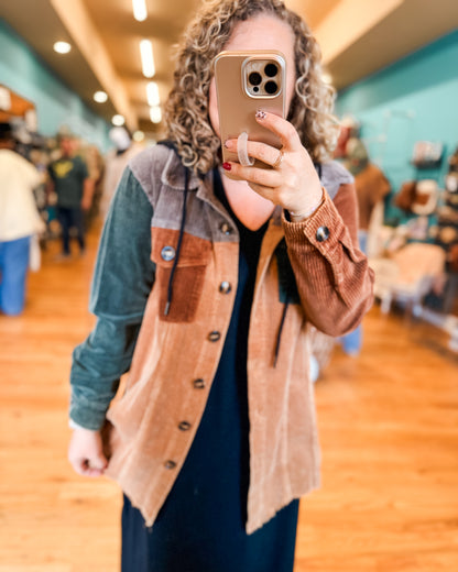 Person taking a mirror selfie wearing a brown and blue jacket in a store.