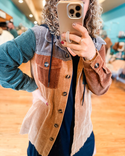 Person wearing a brown corduroy jacket with a checkered shirt underneath, taking a mirror selfie.