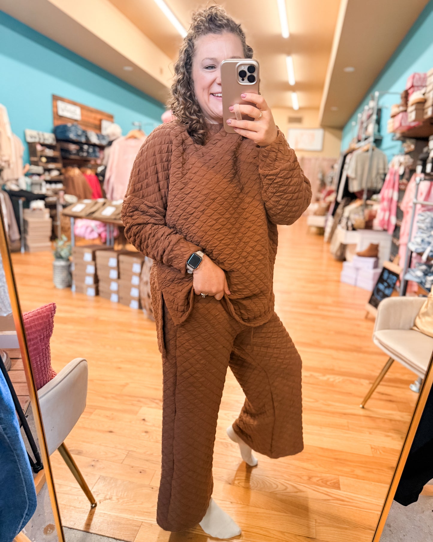 Person wearing a brown textured outfit taking a mirror selfie in a store.