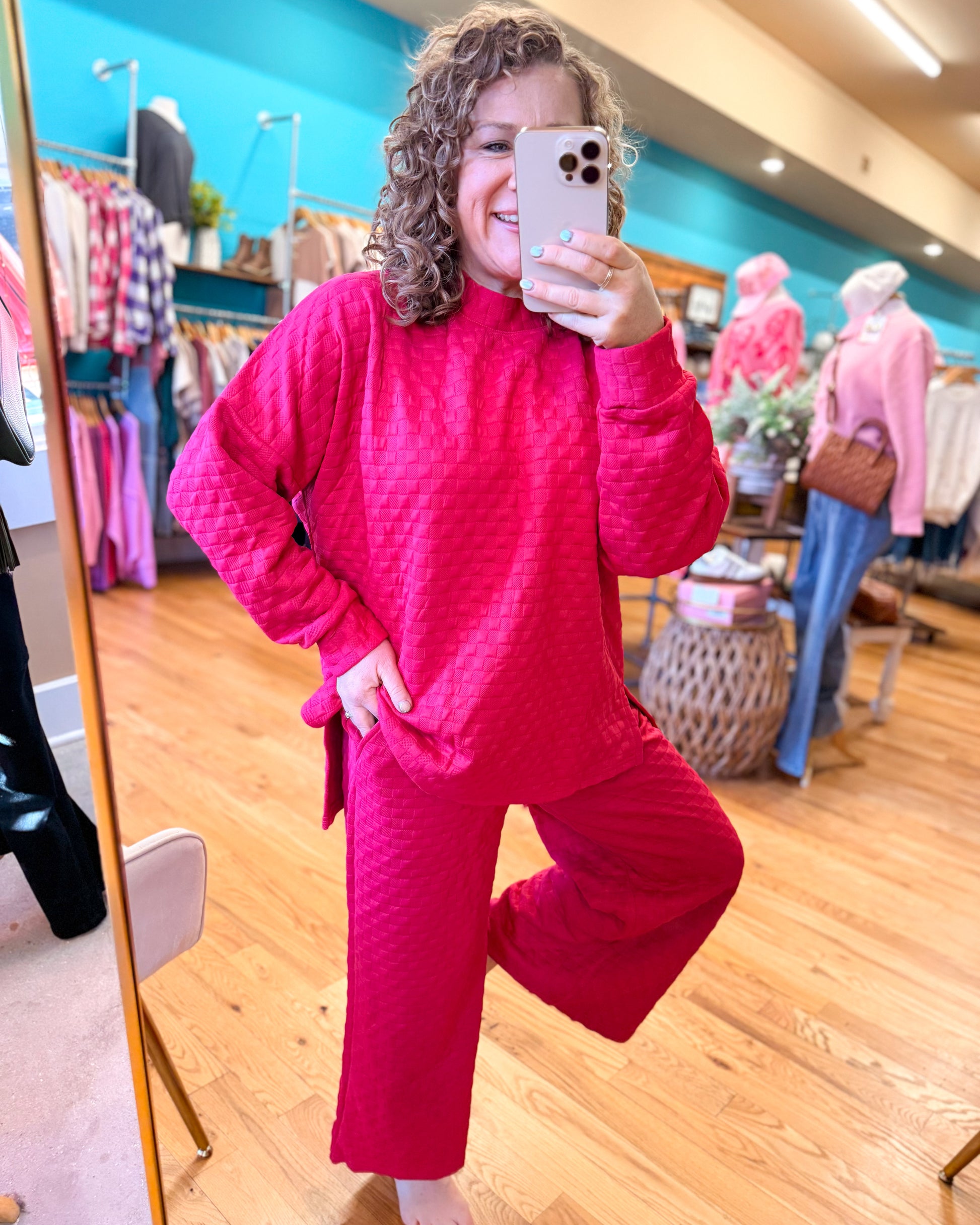 Person wearing a bright pink outfit taking a mirror selfie in a store.