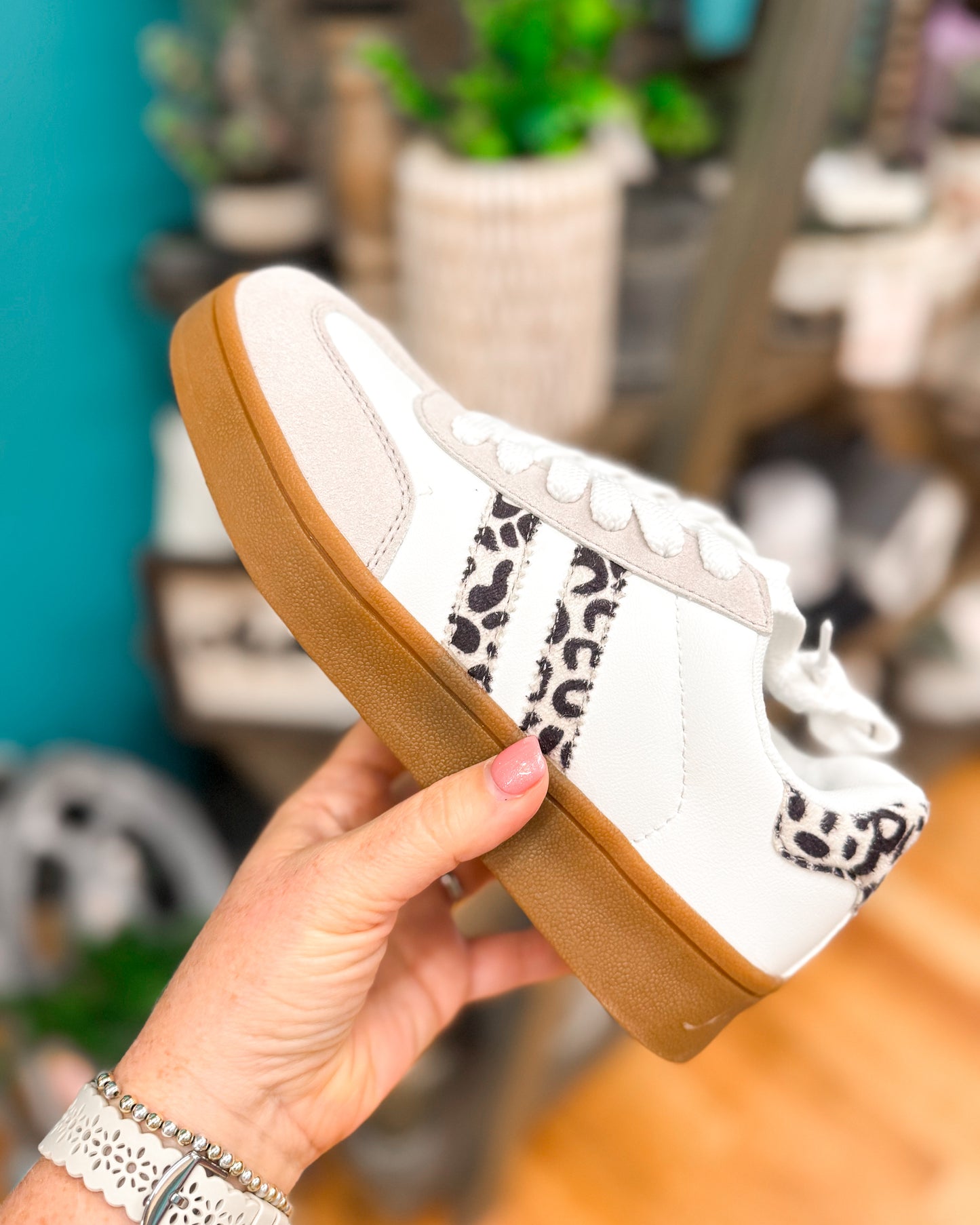 White sneaker with brown sole held by a hand against a blurred indoor background