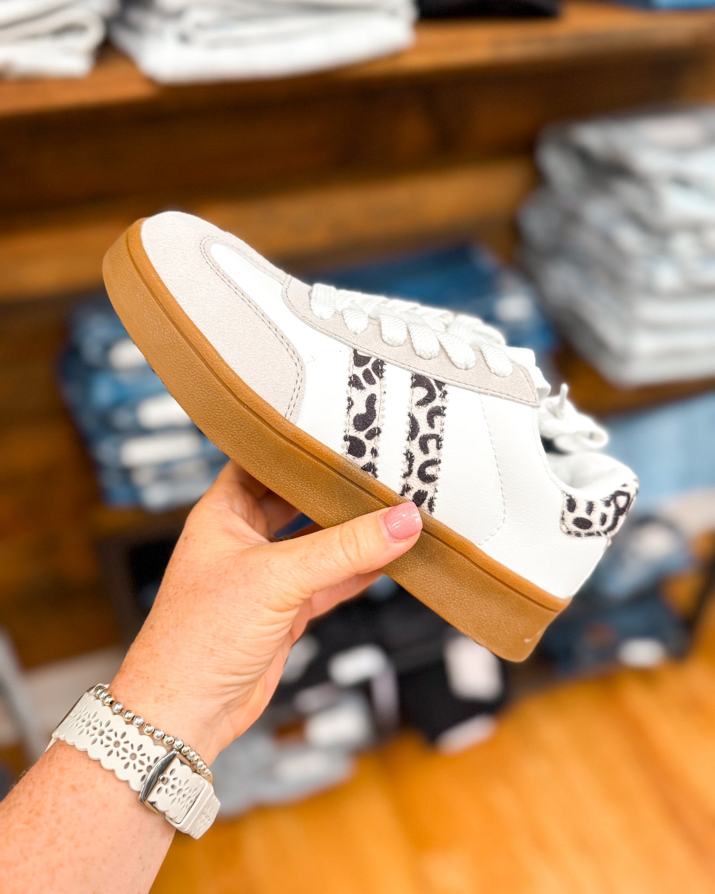 White sneaker with brown sole held by a hand in a store setting