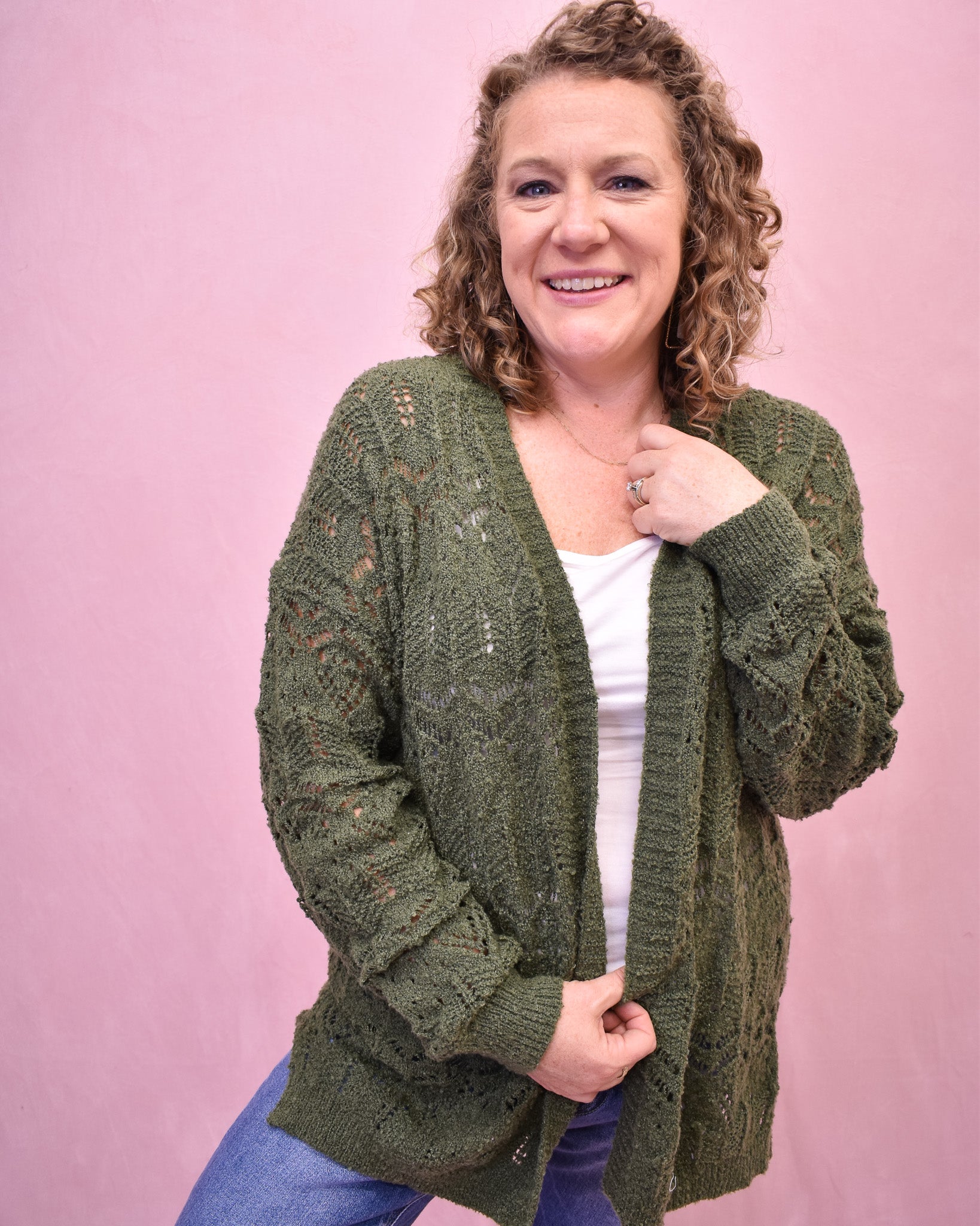 Woman wearing a green knitted cardigan against a pink background
