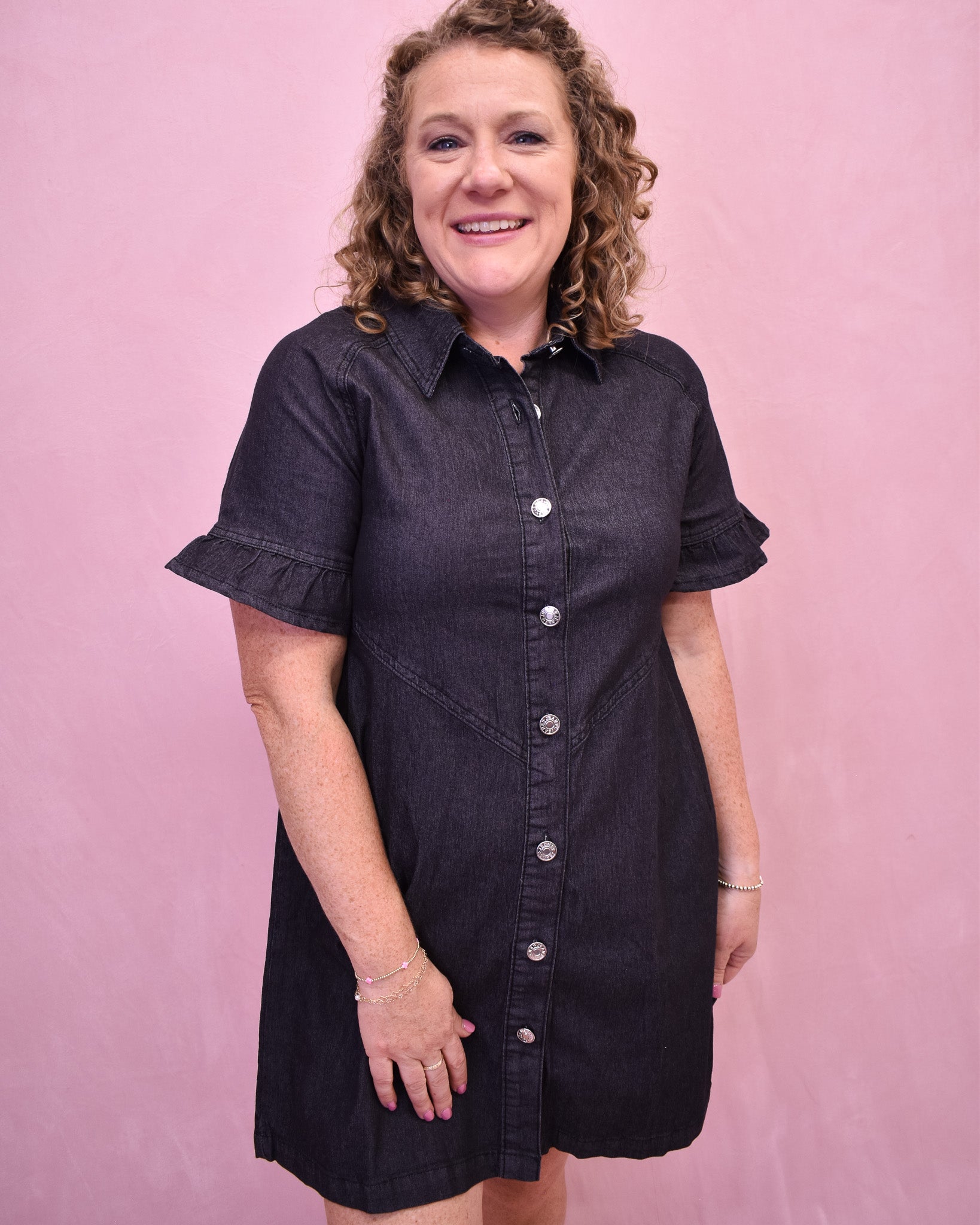 Woman wearing a black denim dress against a pink background