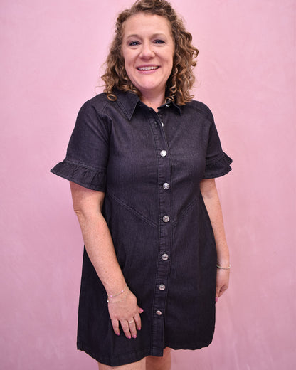 Woman wearing a black denim dress against a pink background