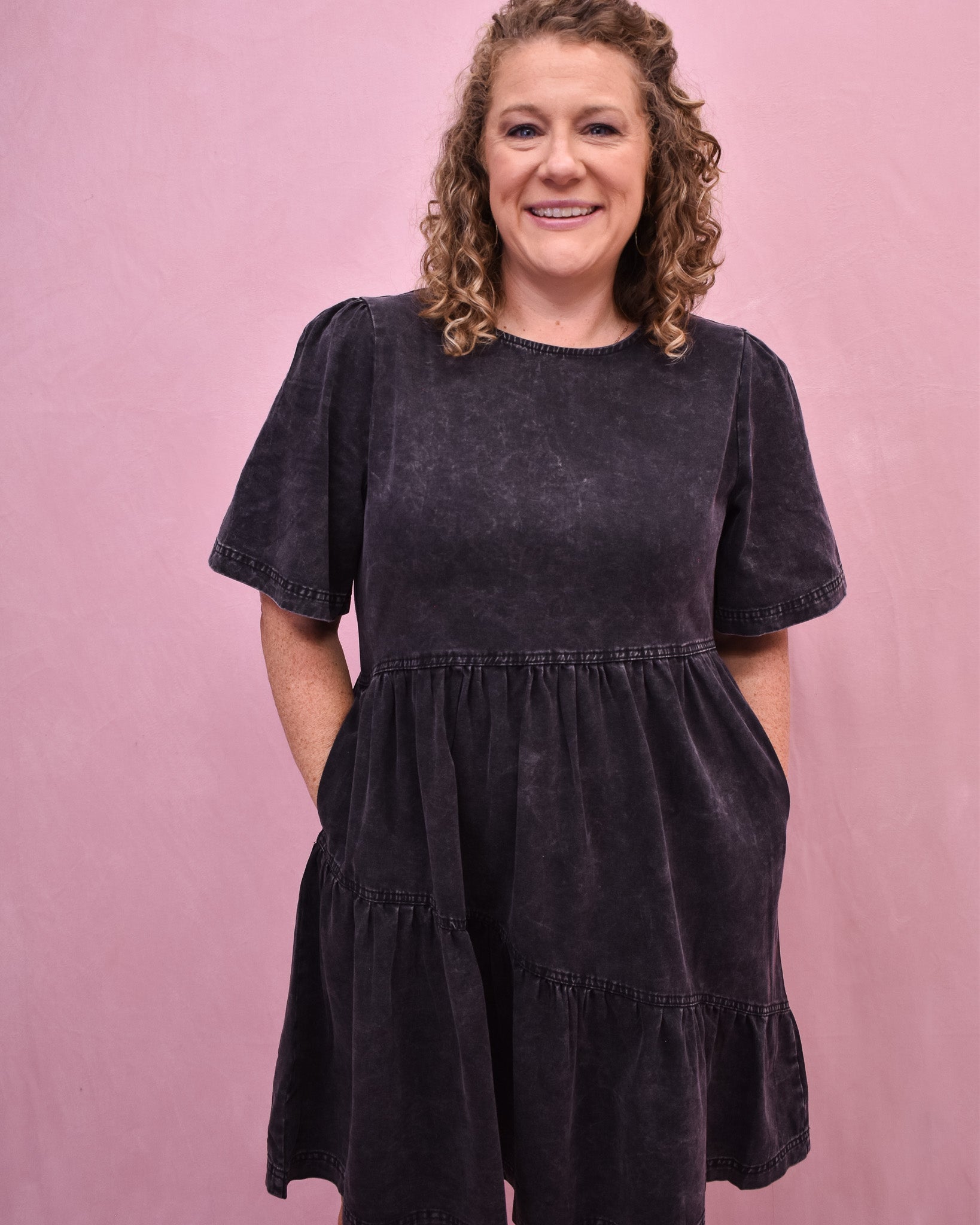 Woman wearing a black tiered dress against a pink background