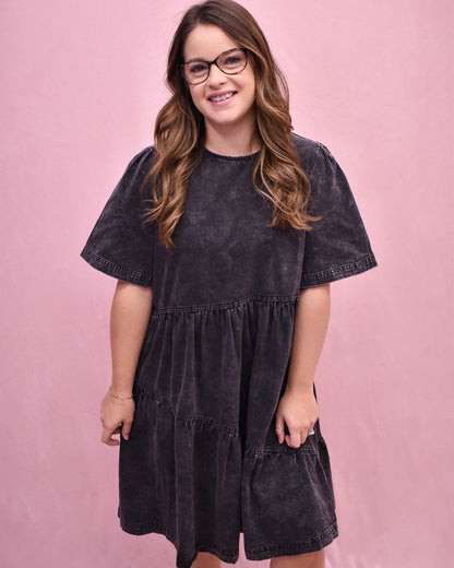 Woman wearing a black tiered dress against a pink background