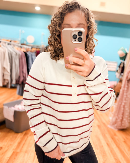 Person wearing a white and red striped sweater taking a mirror selfie in a clothing store.