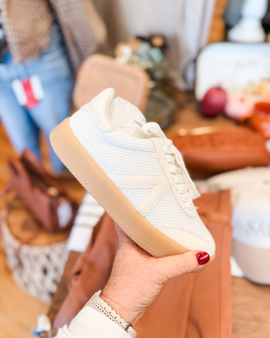 White sneaker held in a hand with a blurred indoor background