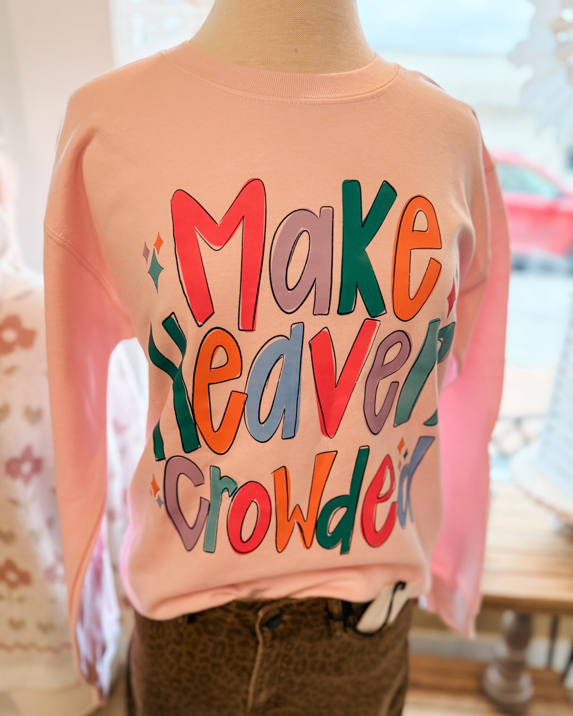 Pink sweatshirt with colorful text on a mannequin against a blurred indoor background