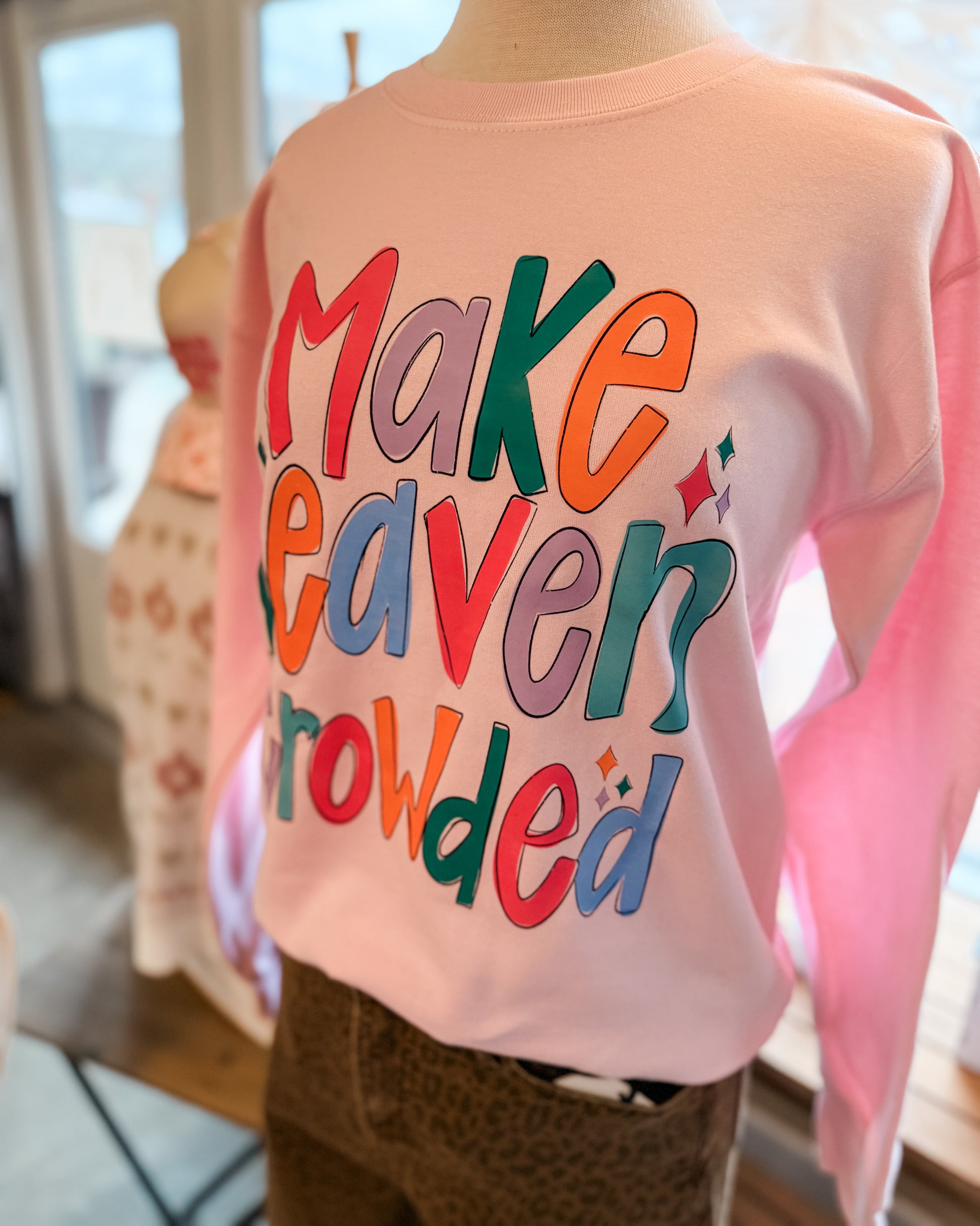 Pink sweatshirt with colorful text worn by a person indoors.