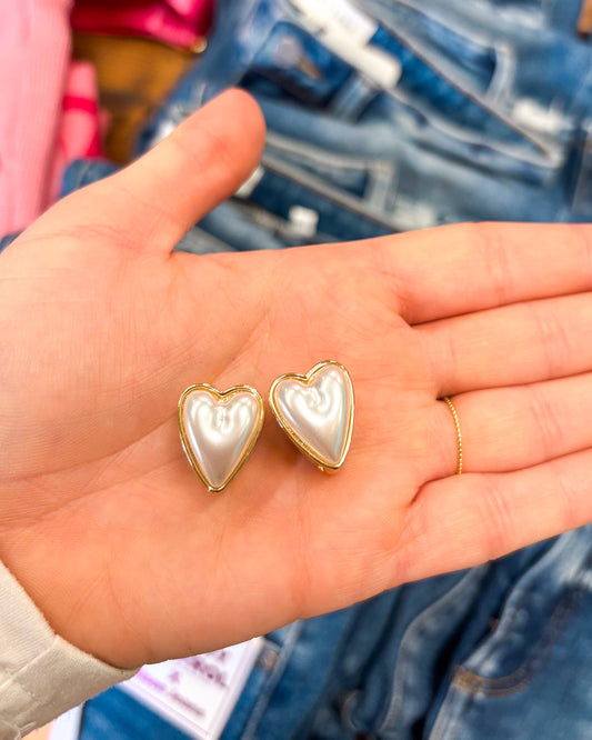 Heart-shaped earrings held in a hand with denim jeans in the background