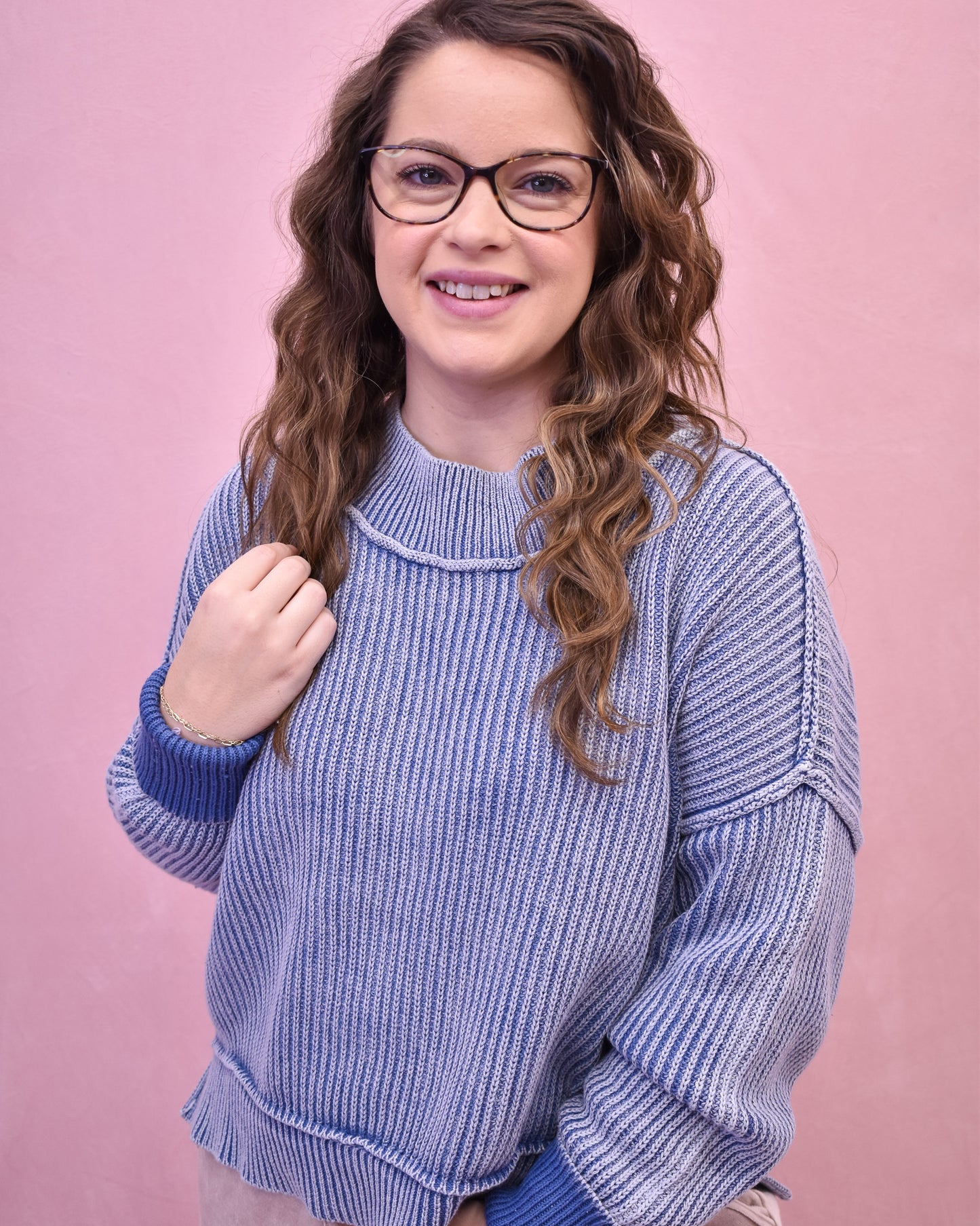 Woman wearing a blue knitted sweater against a pink background