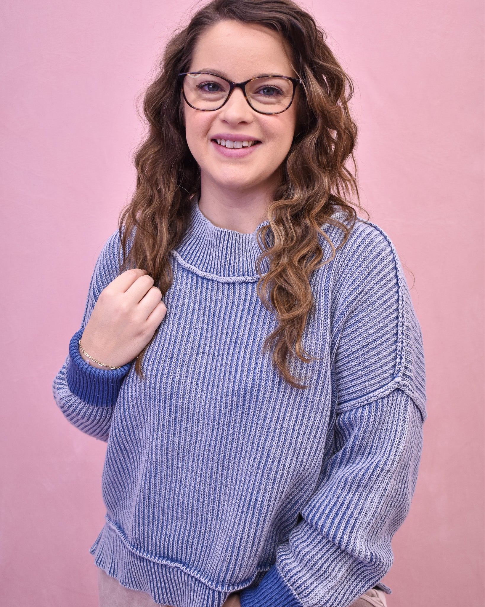 Woman wearing a blue knitted sweater against a pink background