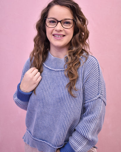Woman wearing a blue knitted sweater against a pink background