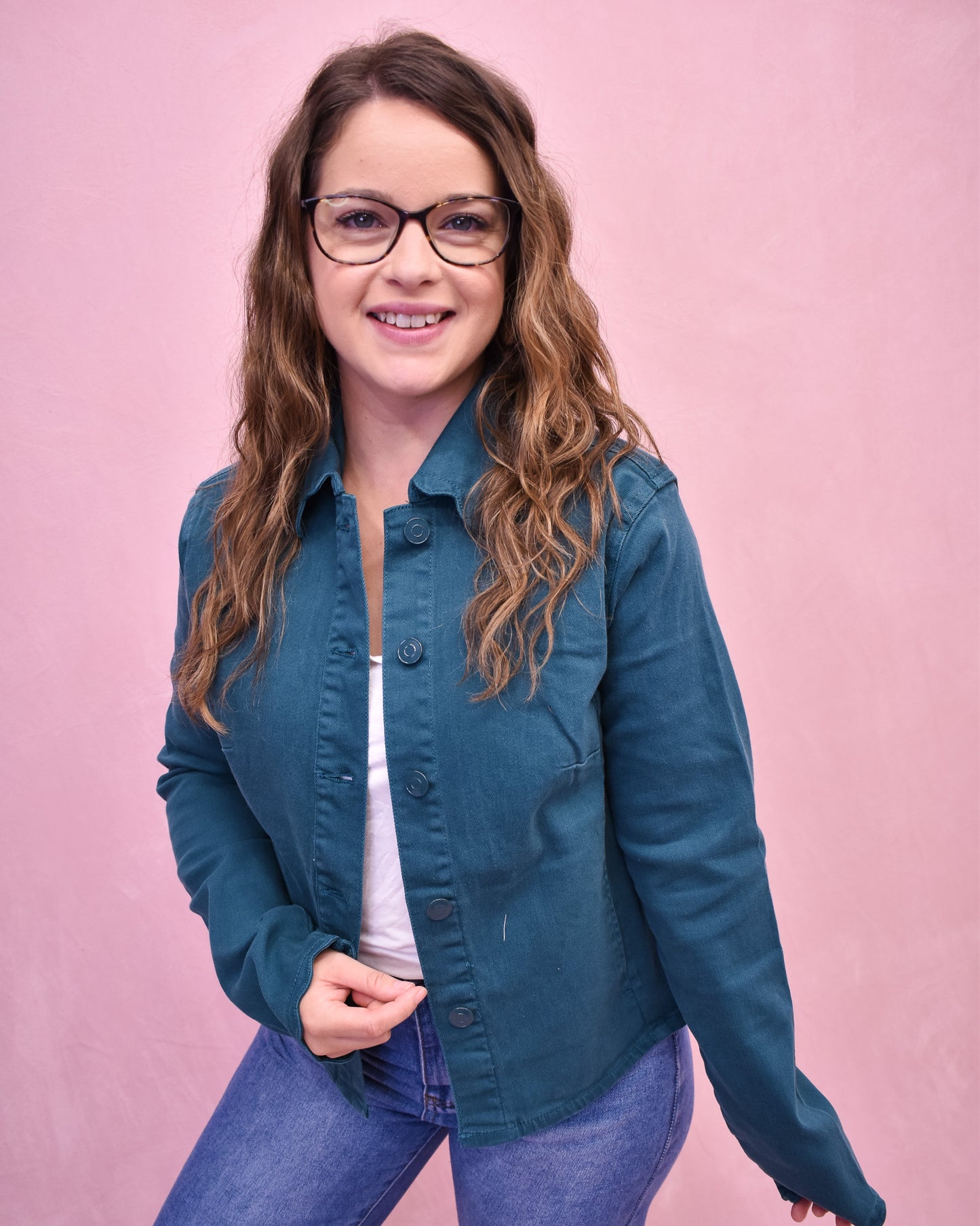 Woman wearing a teal jacket and glasses against a pink background