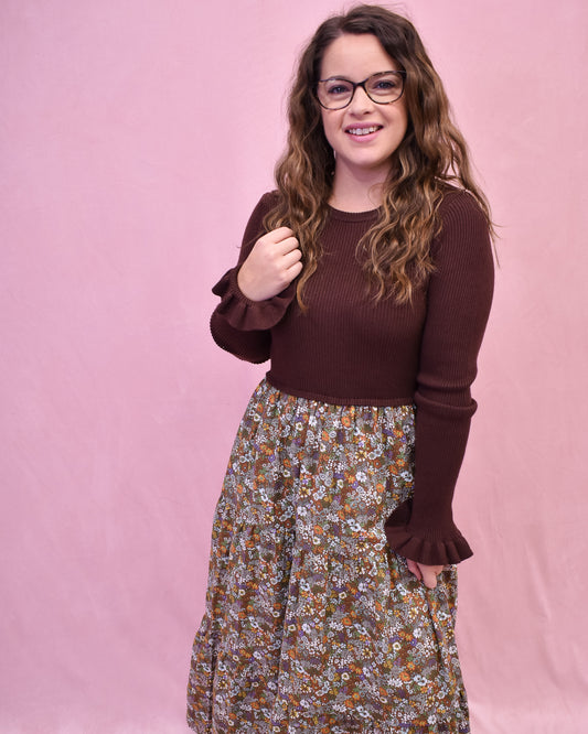 Woman wearing a brown sweater and floral skirt against a pink background