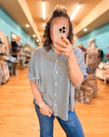 Person taking a mirror selfie in a store wearing a striped shirt and jeans.