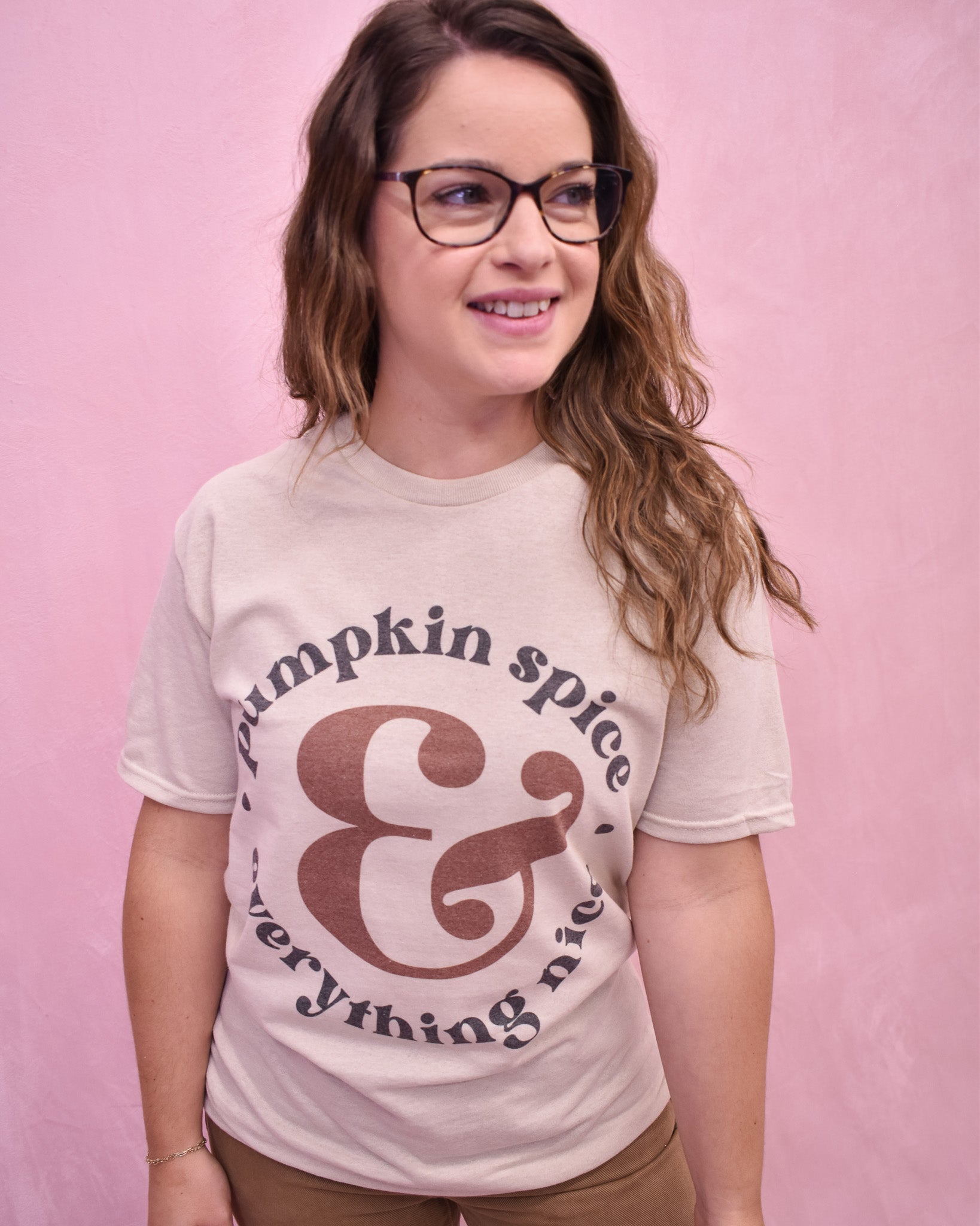 Person wearing a 'Pumpkin spice & everything nice' t-shirt against a pink background