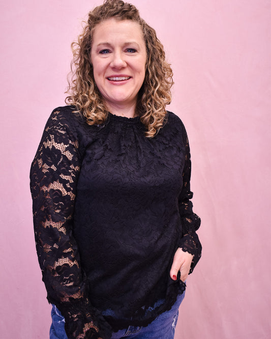 Woman wearing a black lace long-sleeve top against a pink background