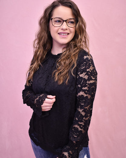 Woman wearing a black lace-sleeve top against a pink background