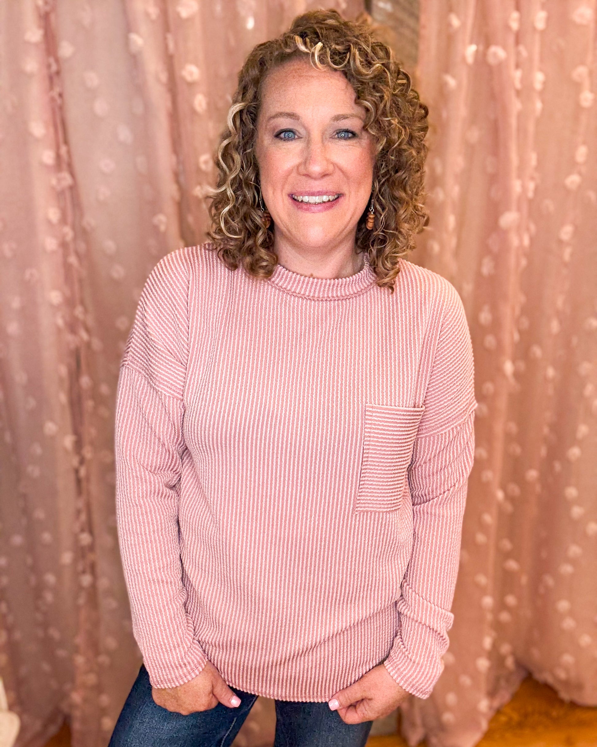 Woman wearing a pink striped sweater in front of a beige curtain