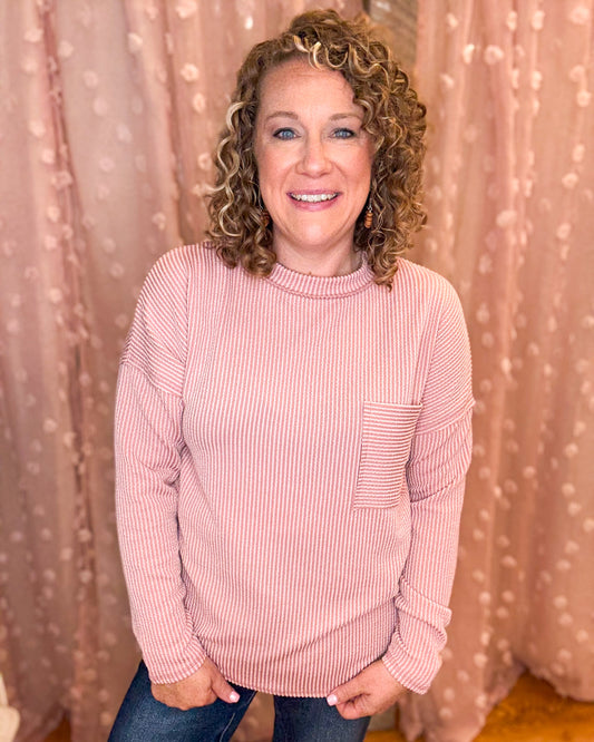 Woman wearing a pink striped sweater in front of a beige curtain