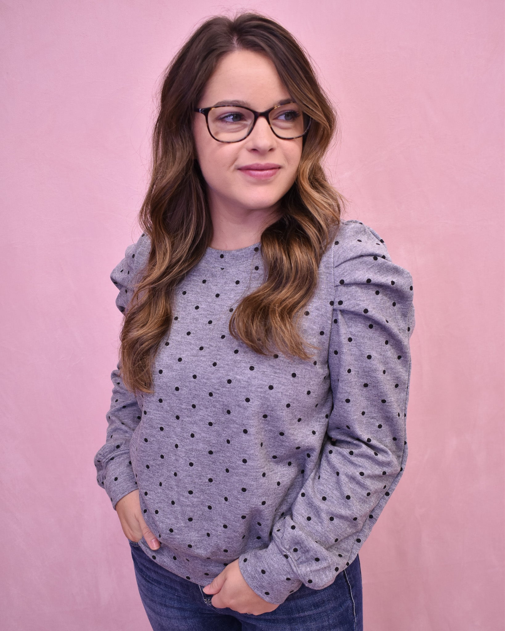 Woman wearing a gray polka dot sweater against a pink background
