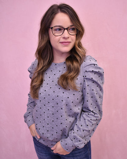 Woman wearing a gray polka dot sweater against a pink background