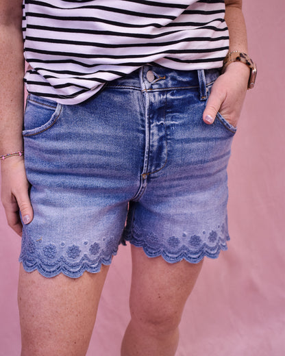 Person wearing blue denim shorts with lace trim and a striped shirt on a pink background