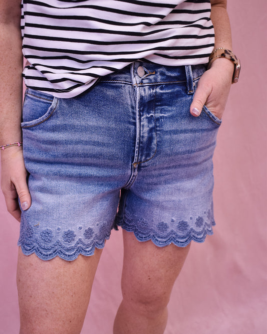 Person wearing blue denim shorts with lace trim and a striped shirt on a pink background