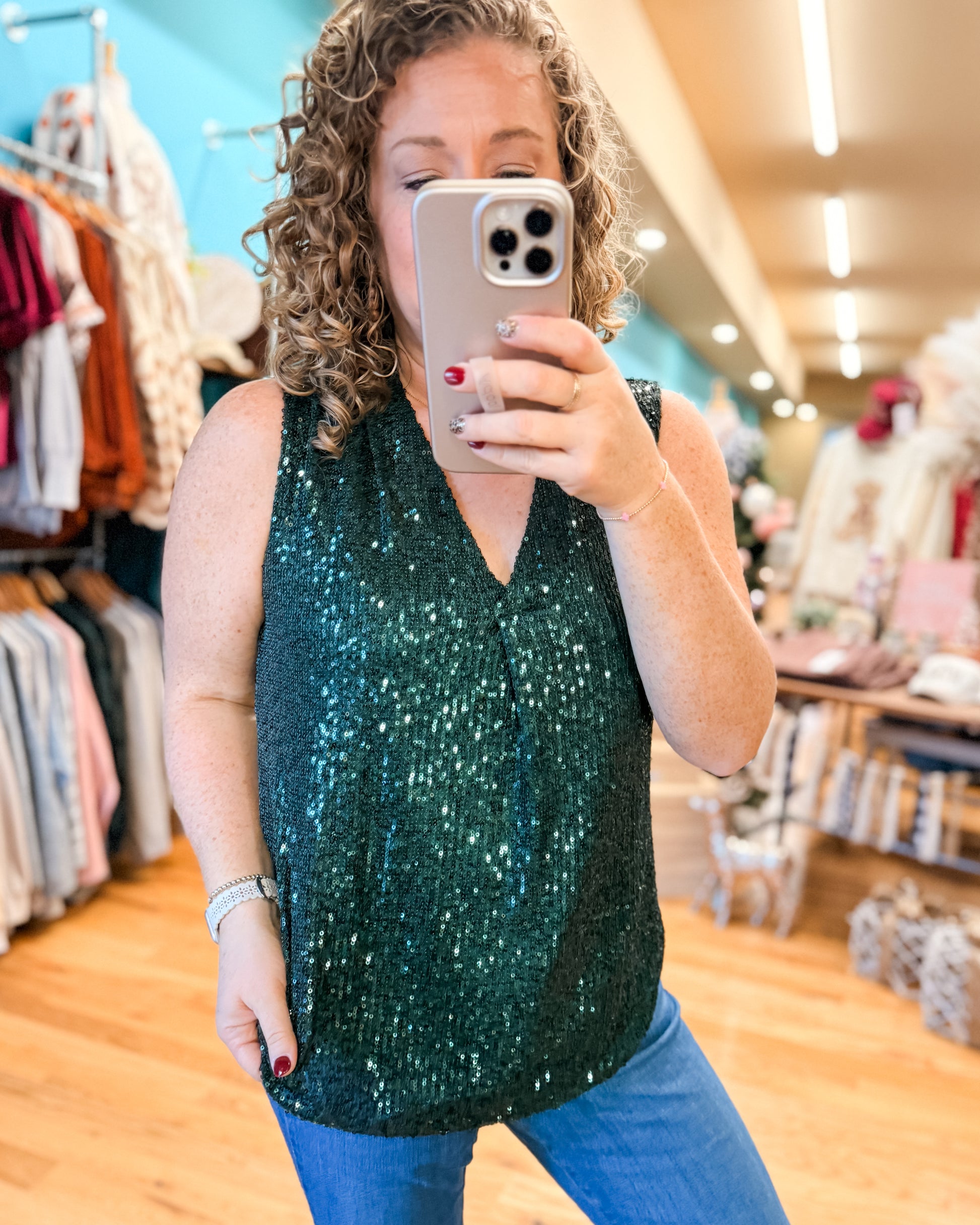 Person taking a mirror selfie wearing a green sequin top in a clothing store.
