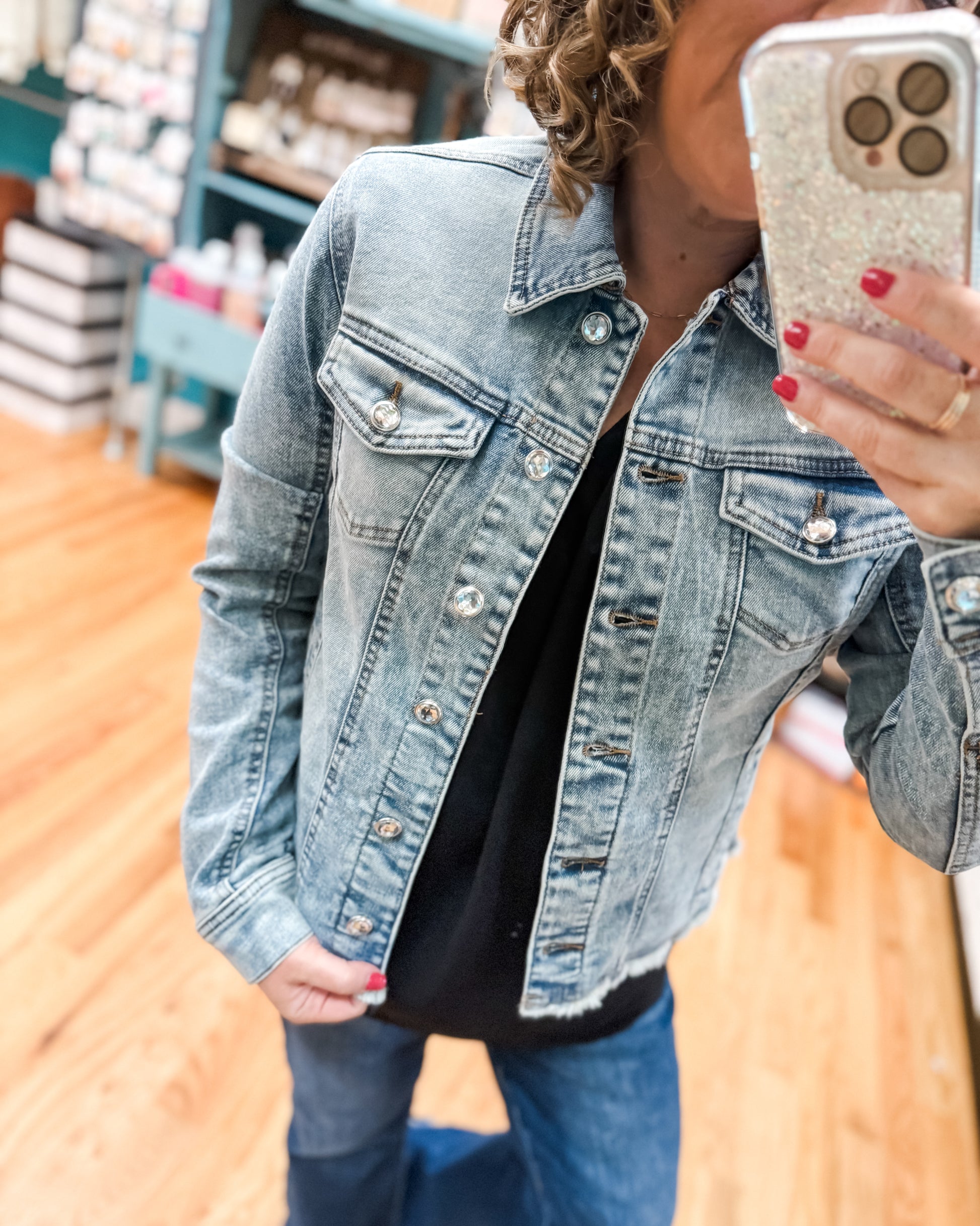 Person wearing a denim jacket taking a selfie with a phone.