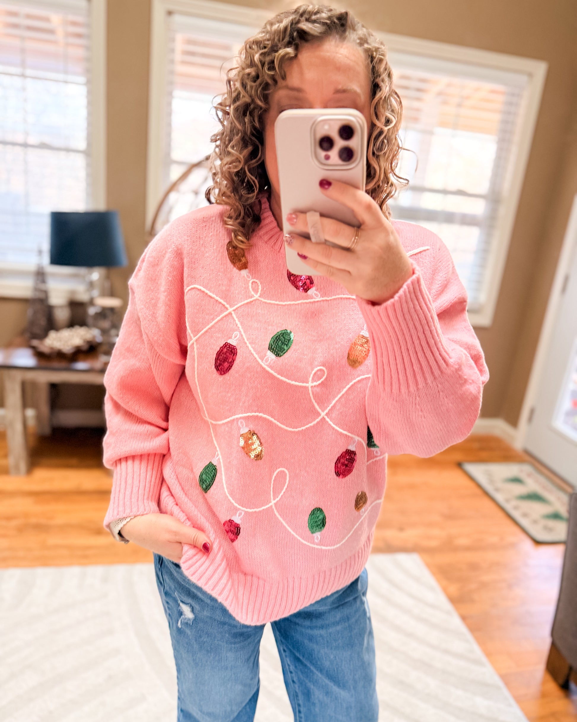 Person wearing a pink sweater with colorful designs, taking a mirror selfie.