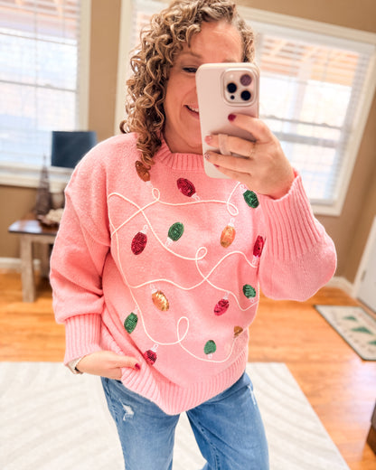 Person wearing a pink sweater with colorful designs, taking a mirror selfie.