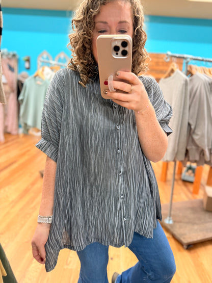 Person taking a mirror selfie wearing a striped shirt and blue jeans in a clothing store.