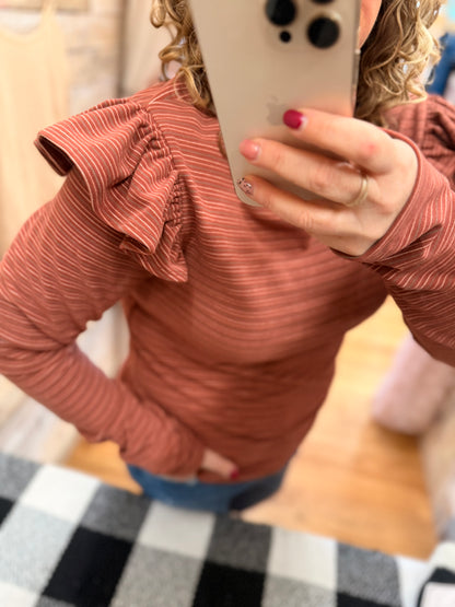 Person wearing a rust-colored long-sleeve top with ruffled details, holding a phone.