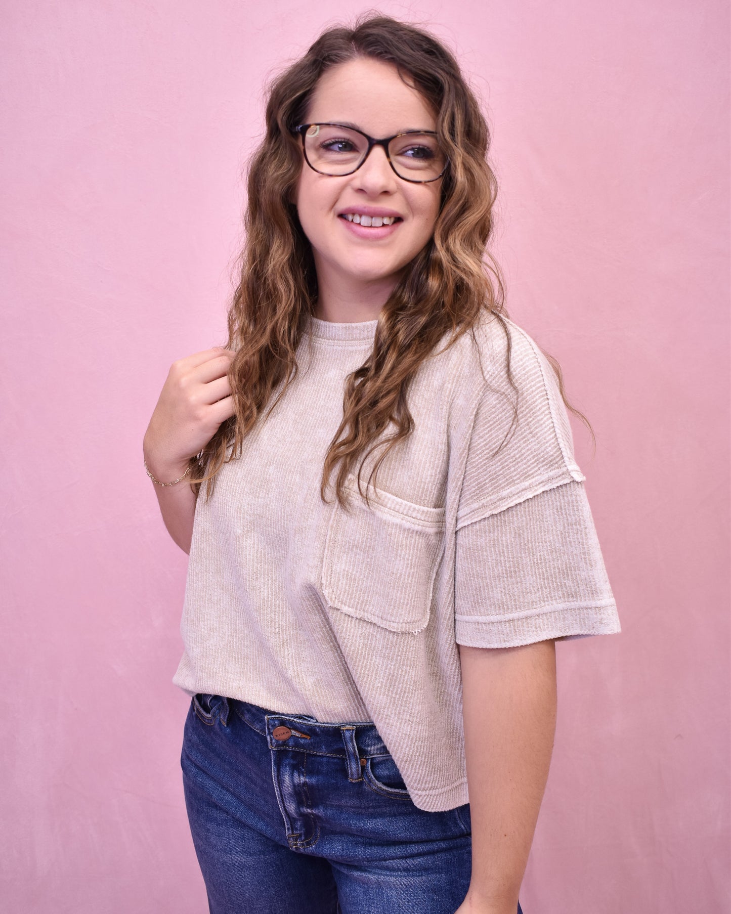 Woman wearing a light-colored top and blue jeans against a pink background