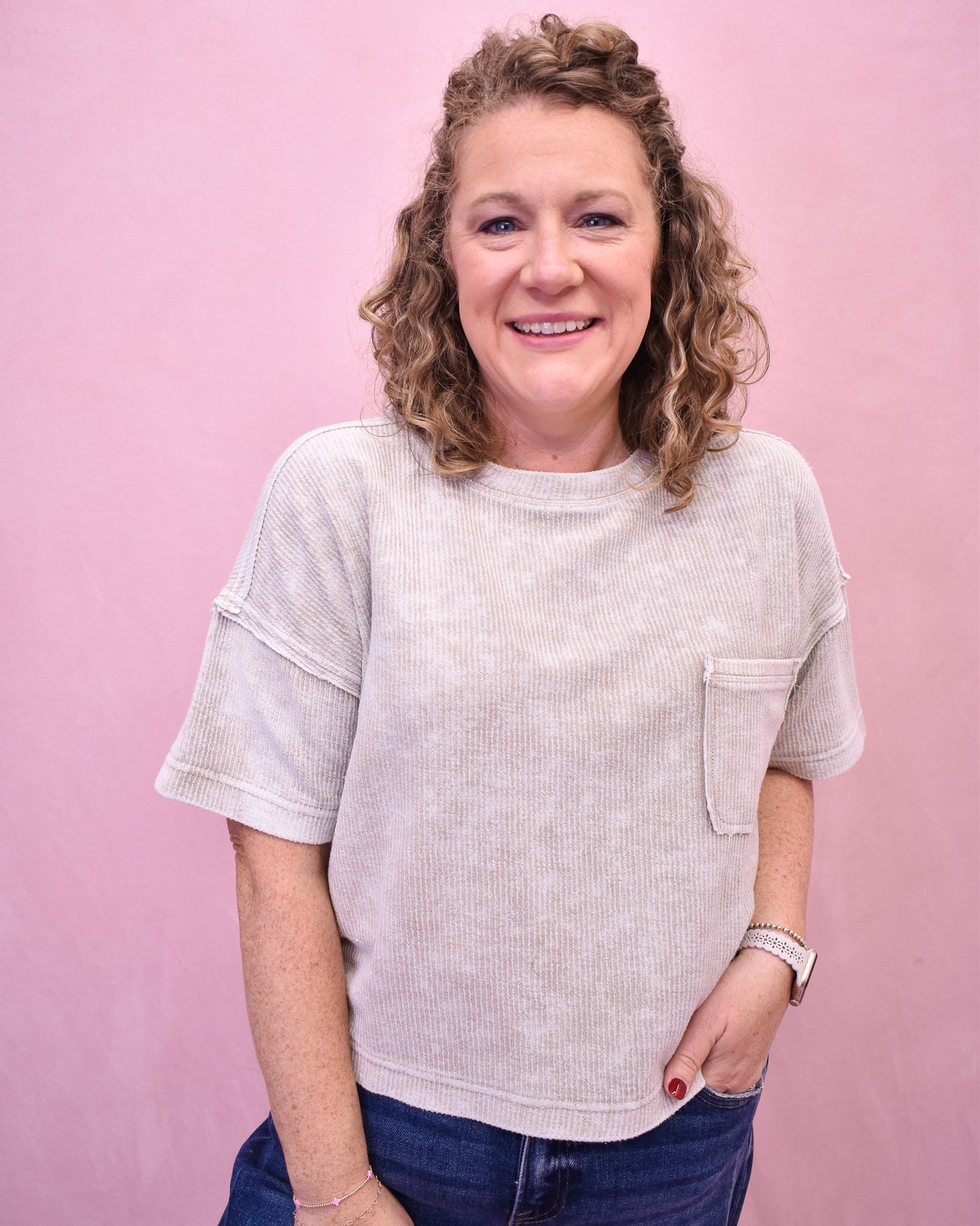 Woman wearing a light-colored t-shirt with a pocket against a pink background