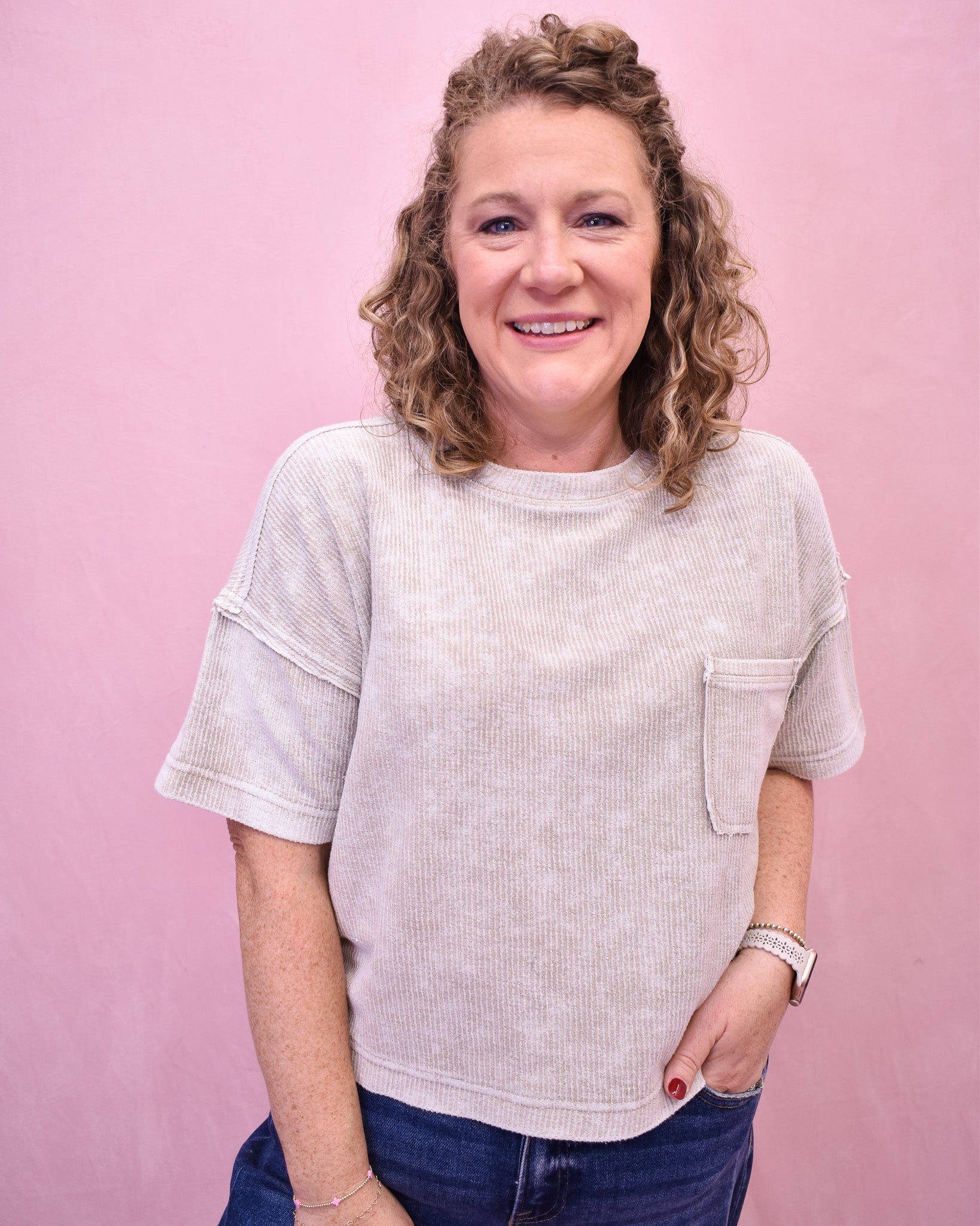 Woman wearing a light-colored t-shirt with a pocket against a pink background